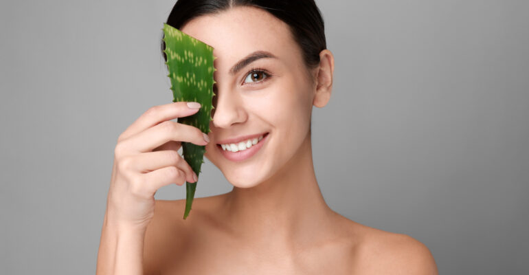 Portrait of beautiful woman with aloe vera on grey background